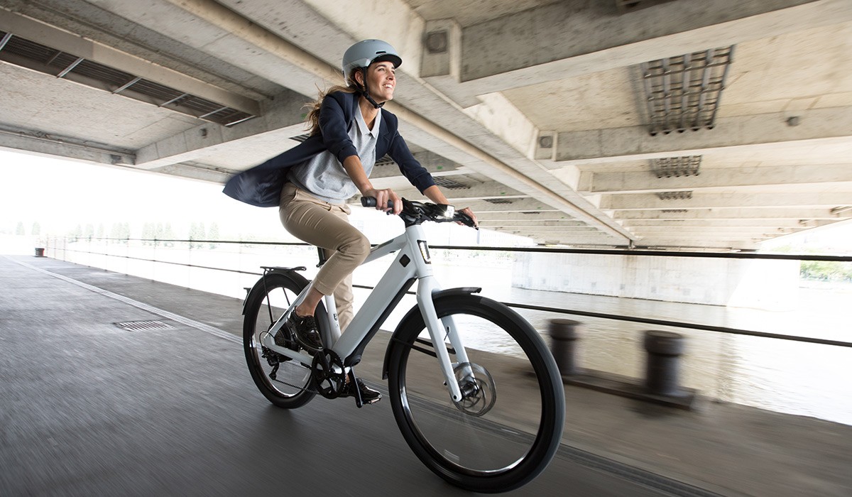 Ontspannen en veilig onderweg met e-bikeverzekering: vrouw rijdt op haar Stromer e-bike langs een rivier.